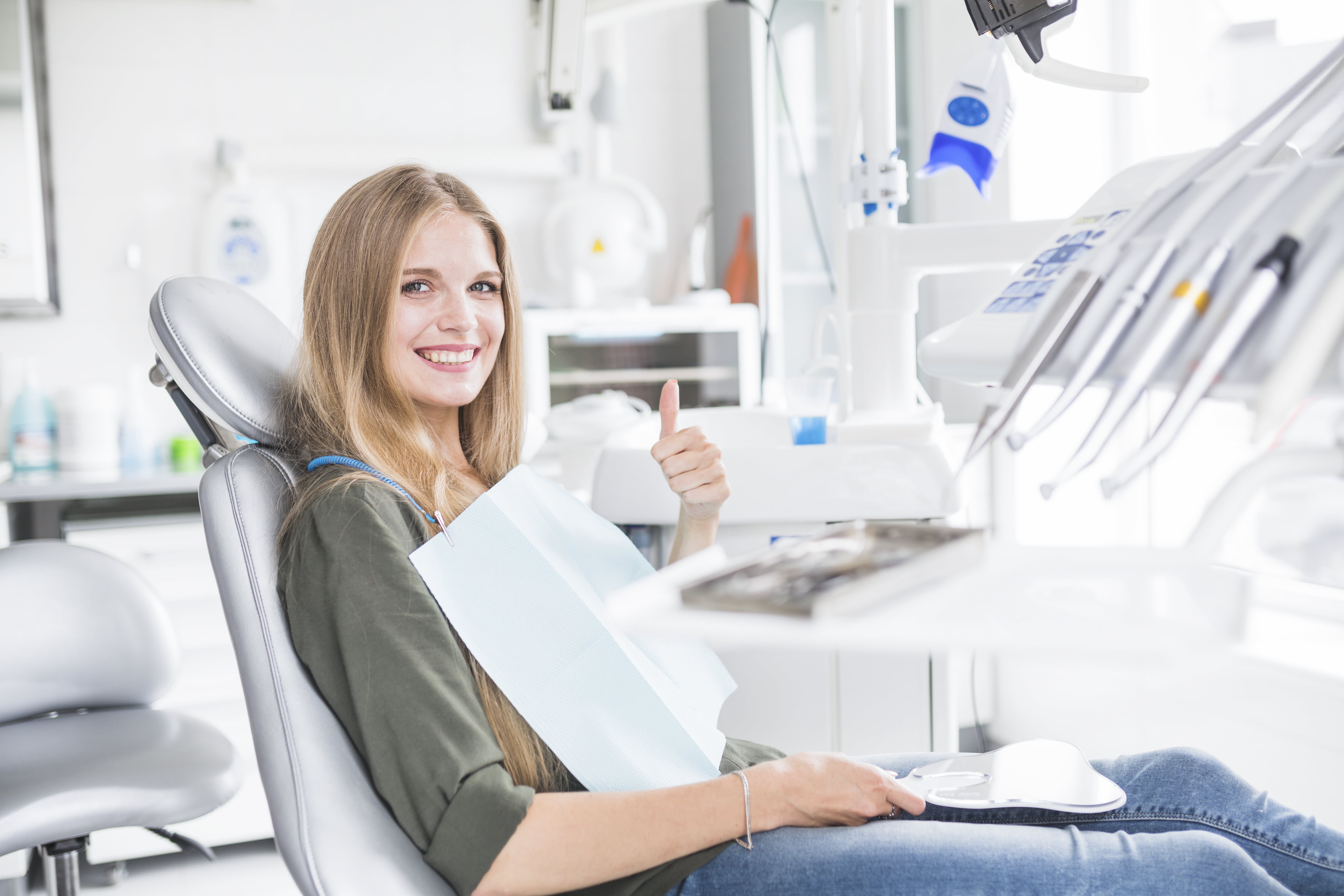Mulher sentada em cadeira de dentista sorrindo como polegar levantado